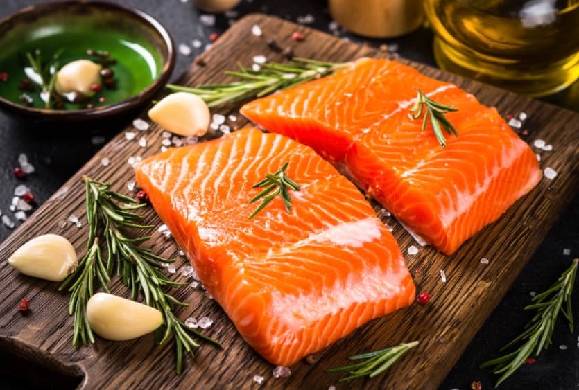 Fresh salmon fillets on a wooden board with rosemary and garlic