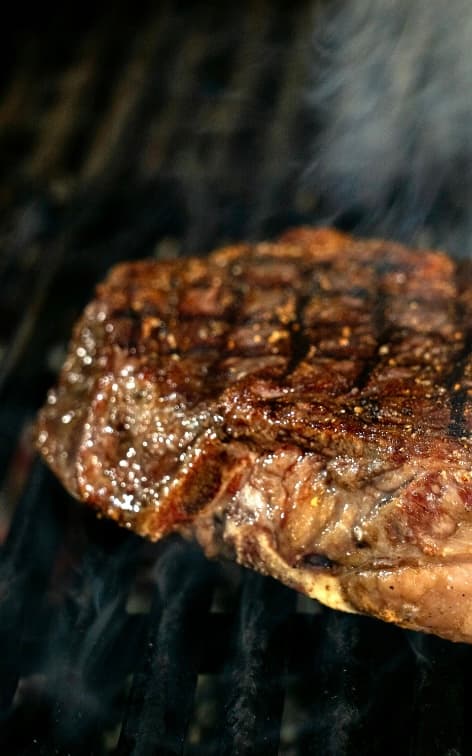 A thick steak searing on the grill with rising smoke